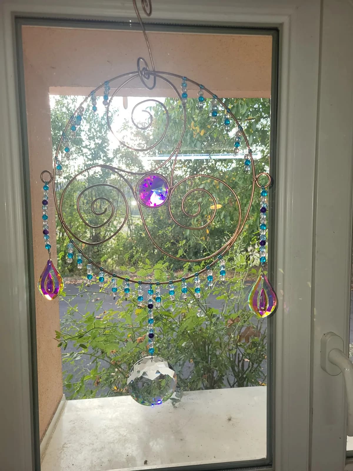 L’éveil des spirales, suspension artisanale en cuivre avec perles turquoise et prismes devant une fenêtre